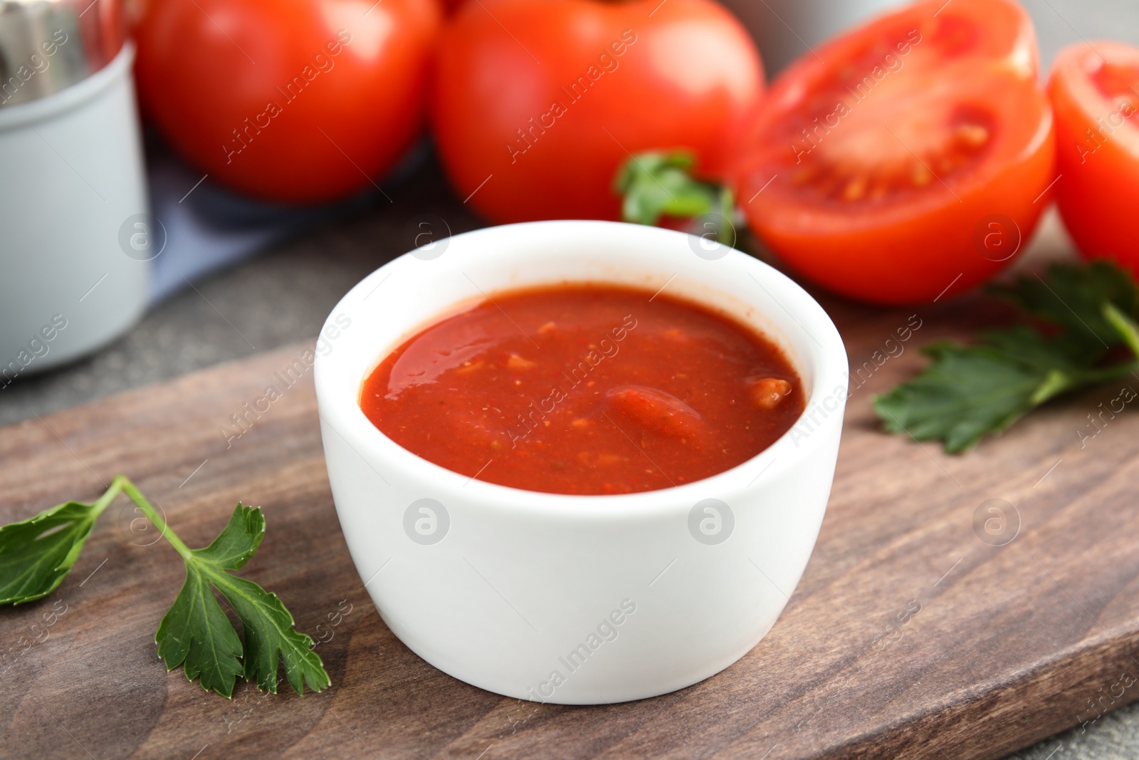 Photo of Wooden board with bowl of tomato sauce and parsley on table