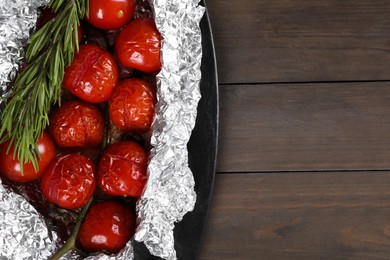 Aluminum foil with delicious baked tomatoes and rosemary on wooden table, top view. Space for text