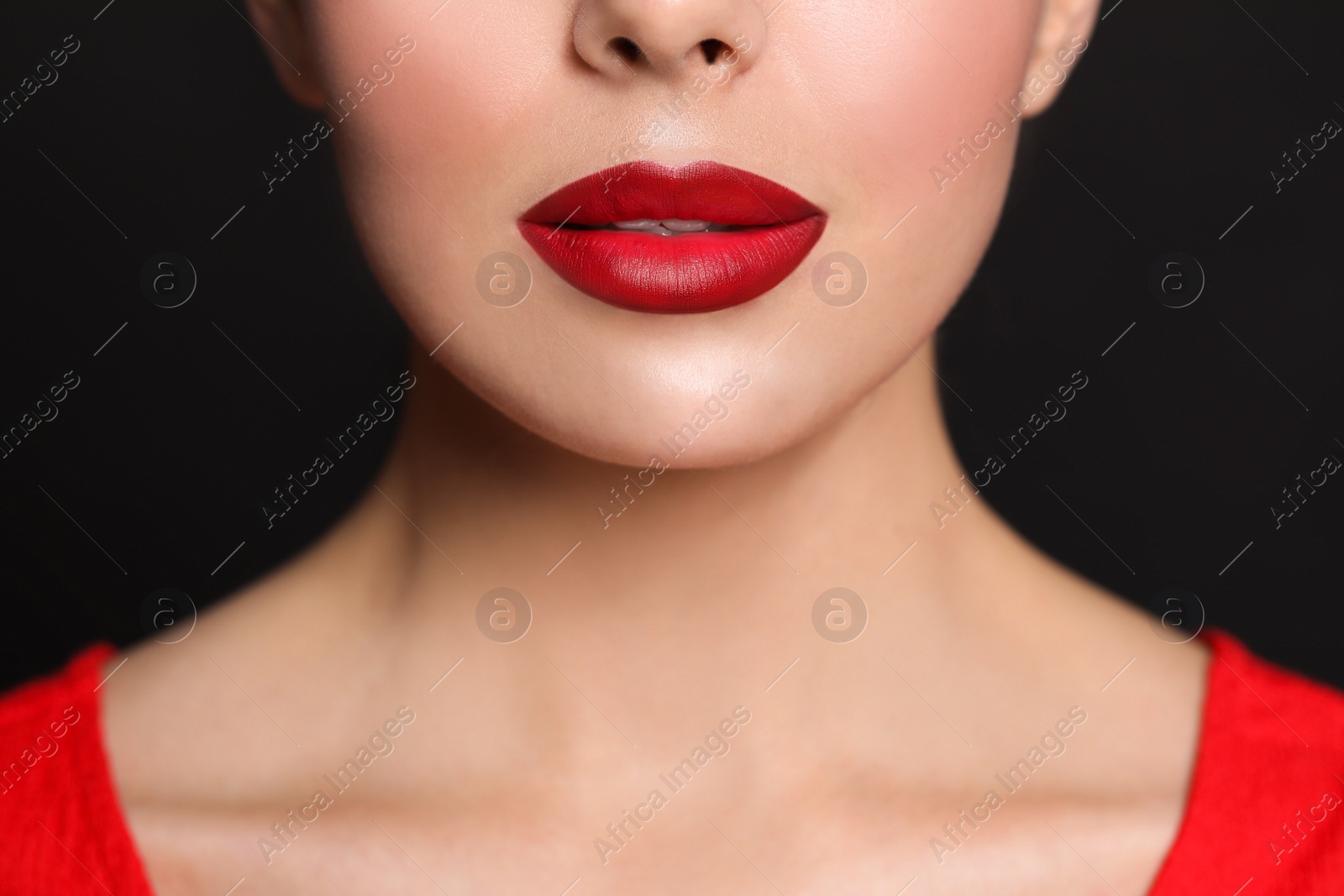 Photo of Young woman wearing beautiful red lipstick on black background, closeup