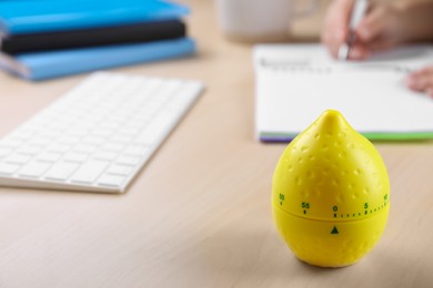 Woman writing in notebook at wooden table, focus on kitchen timer in shape of lemon. Space for text