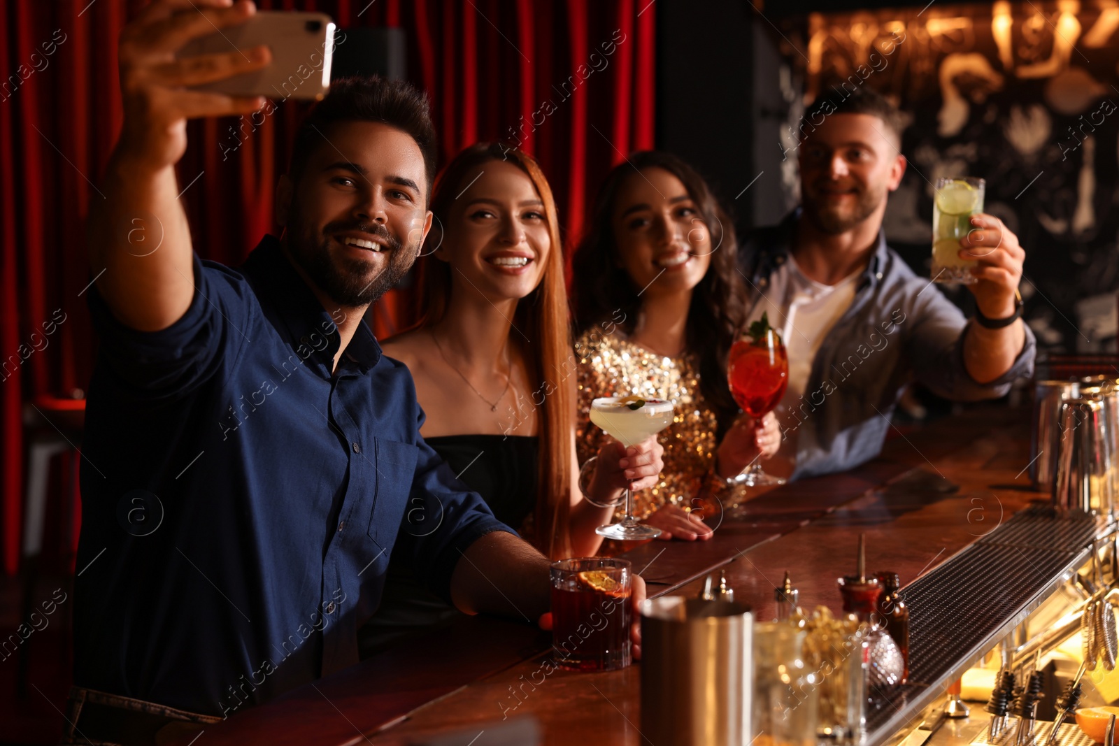 Photo of Happy friends with cocktails taking selfie together in bar