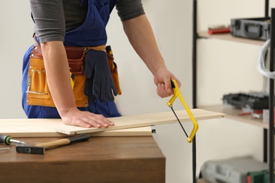 Photo of Young working man using hand saw indoors, closeup. Home repair