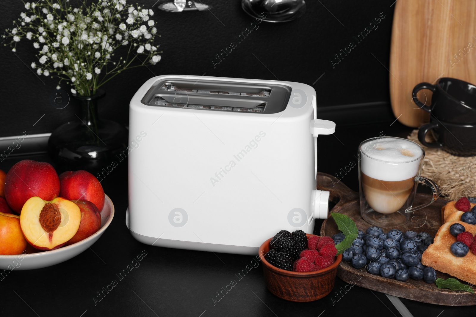 Photo of Modern toaster, bread, fresh berries and coffee on black table