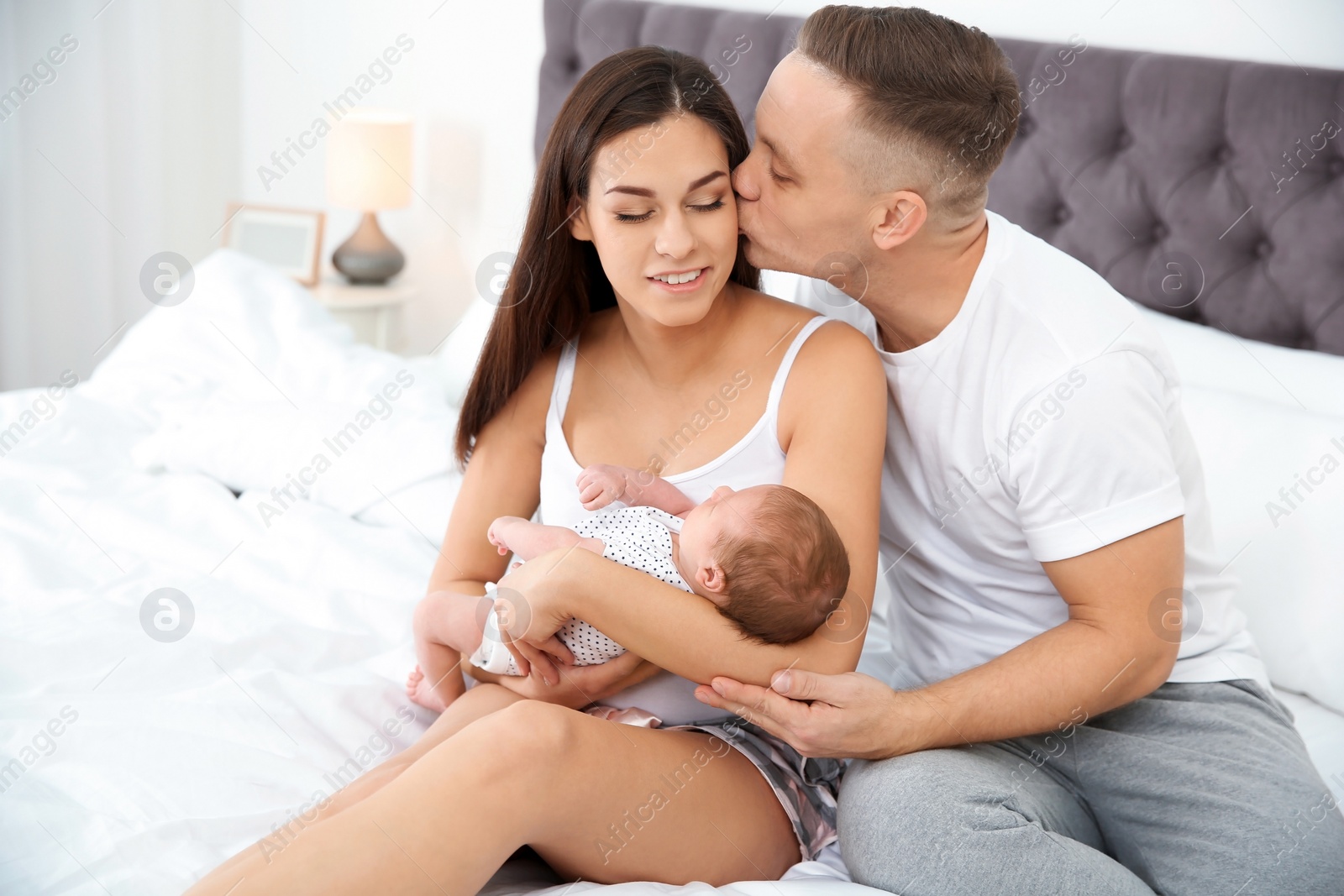 Photo of Happy couple with their newborn baby on bed