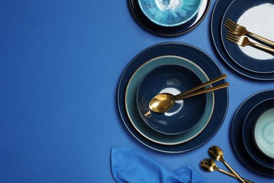 Photo of Clean dishware and cutlery on blue background, flat lay. Space for text