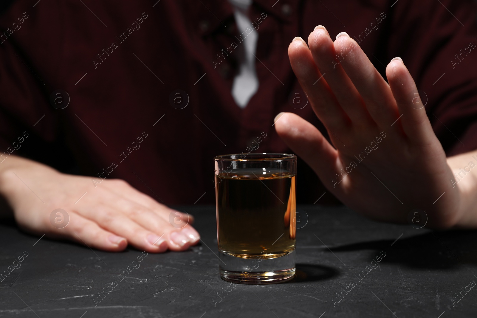 Photo of Alcohol addiction. Woman refusing glass of whiskey at dark textured table, closeup
