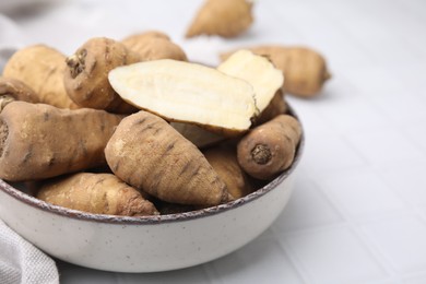 Photo of Whole and cut tubers of turnip rooted chervil in bowl on white tiled table, closeup