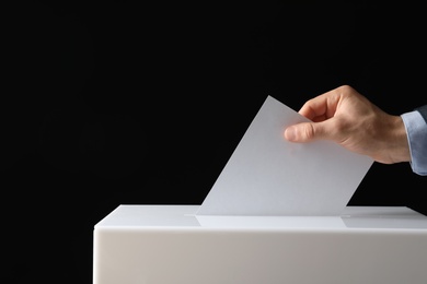 Photo of Man putting his vote into ballot box on black background, closeup