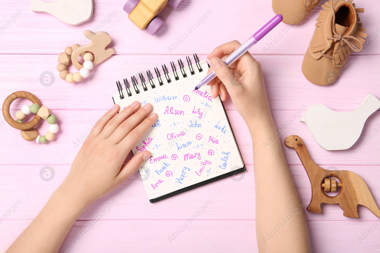 Photo of Woman choosing baby name at pink wooden table, top view