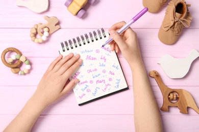 Woman choosing baby name at pink wooden table, top view