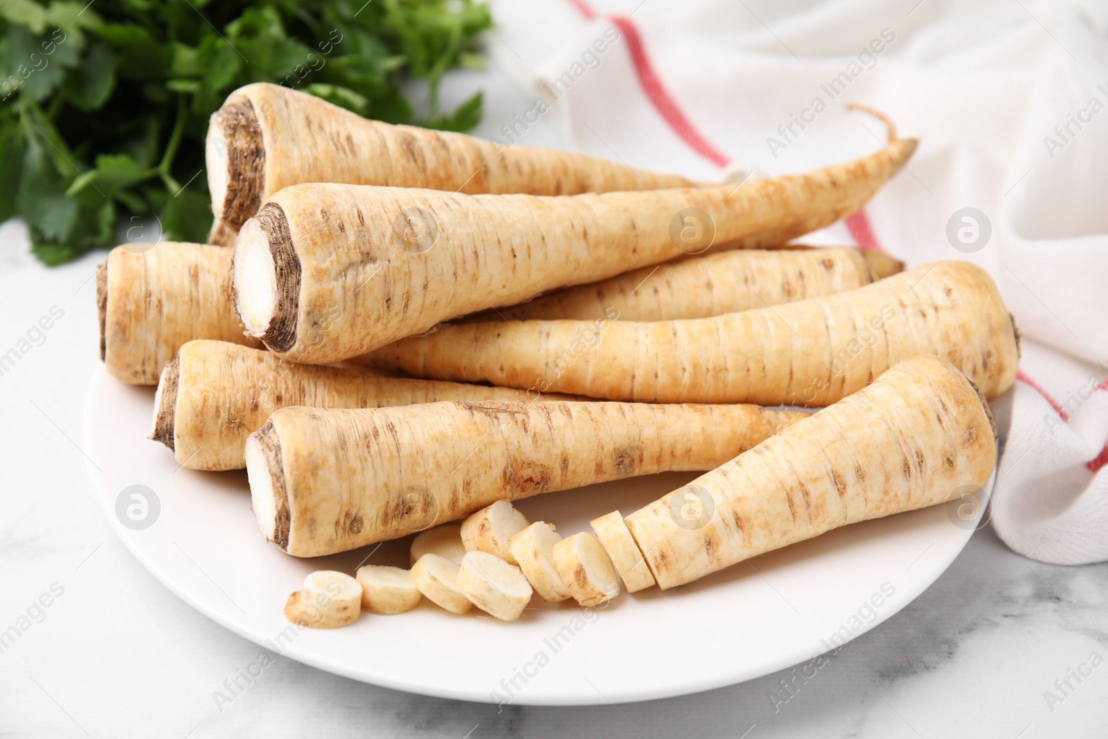 Photo of Plate with whole and cut parsley roots on white table, closeup