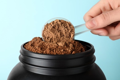 Man taking protein powder with scoop from jar against color background, closeup