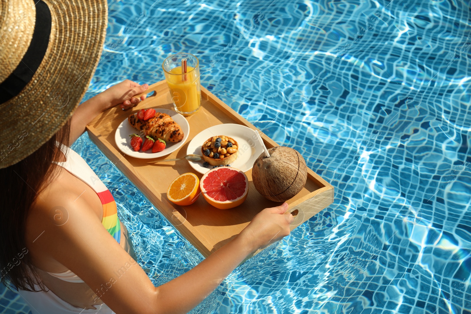 Photo of Young woman with delicious breakfast on tray in swimming pool, closeup