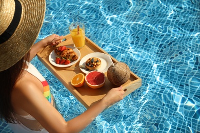 Young woman with delicious breakfast on tray in swimming pool, closeup