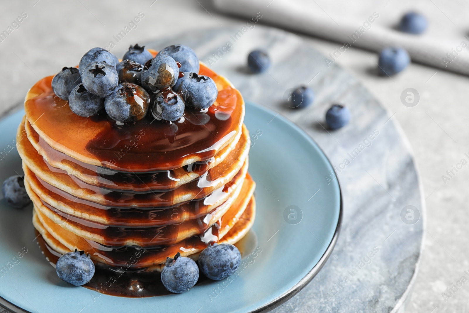Photo of Plate of delicious pancakes with fresh blueberries and syrup on light grey table, closeup