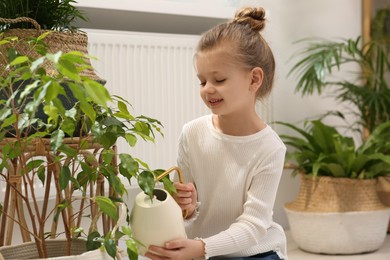 Photo of Cute little girl watering beautiful green plant at home. House decor