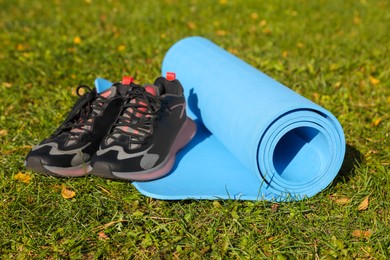 Photo of Bright karemat or fitness mat and sportive shoes on fresh green grass outdoors