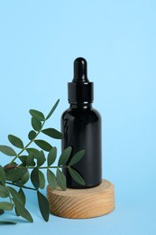 Photo of Bottle with cosmetic oil on podium and green twig on light blue background