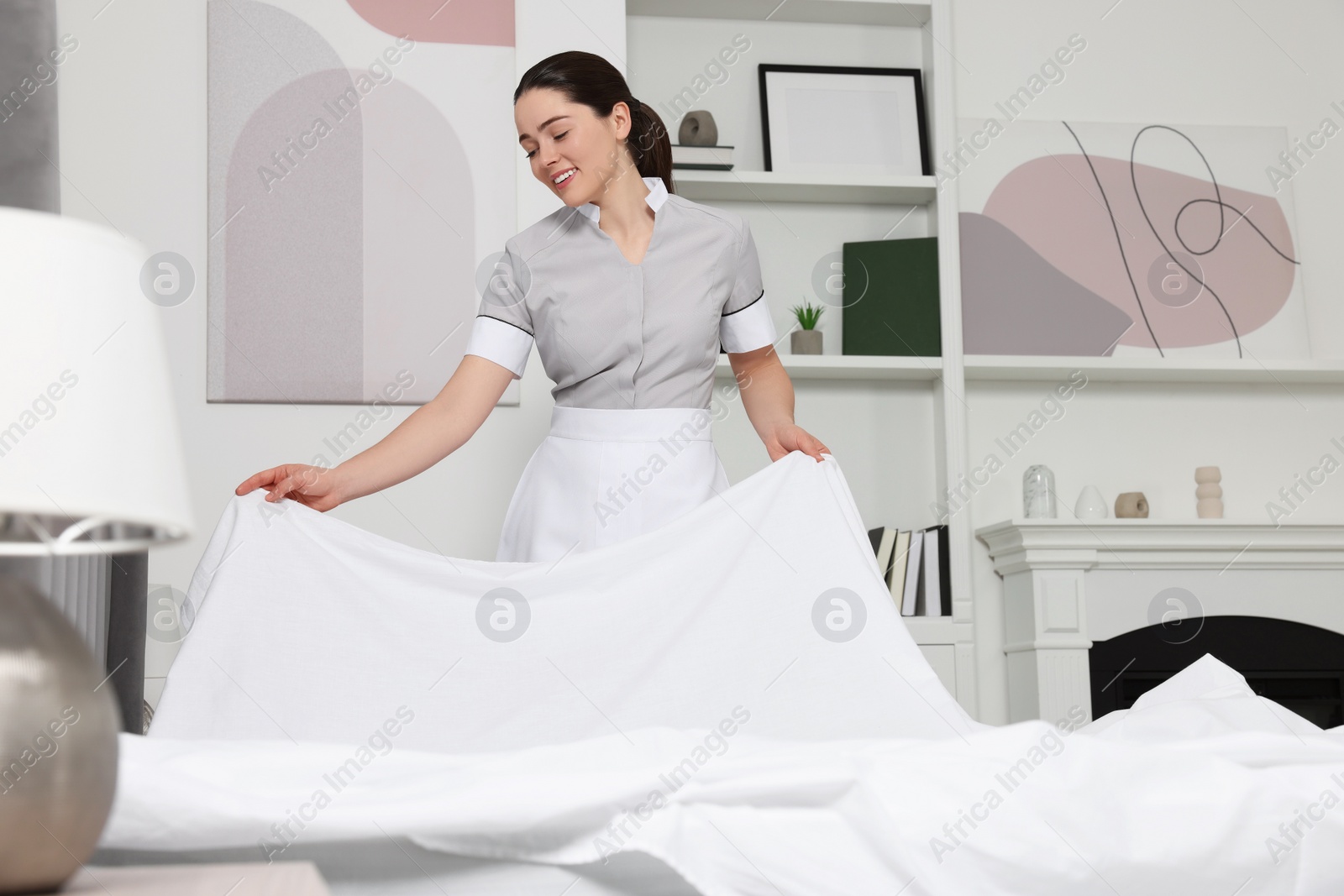 Photo of Young maid making bed in hotel room