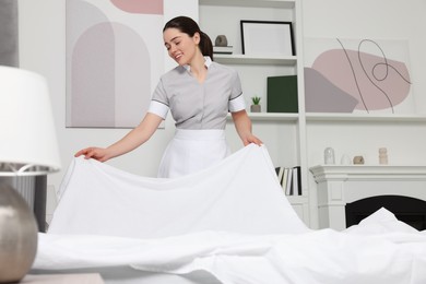 Photo of Young maid making bed in hotel room