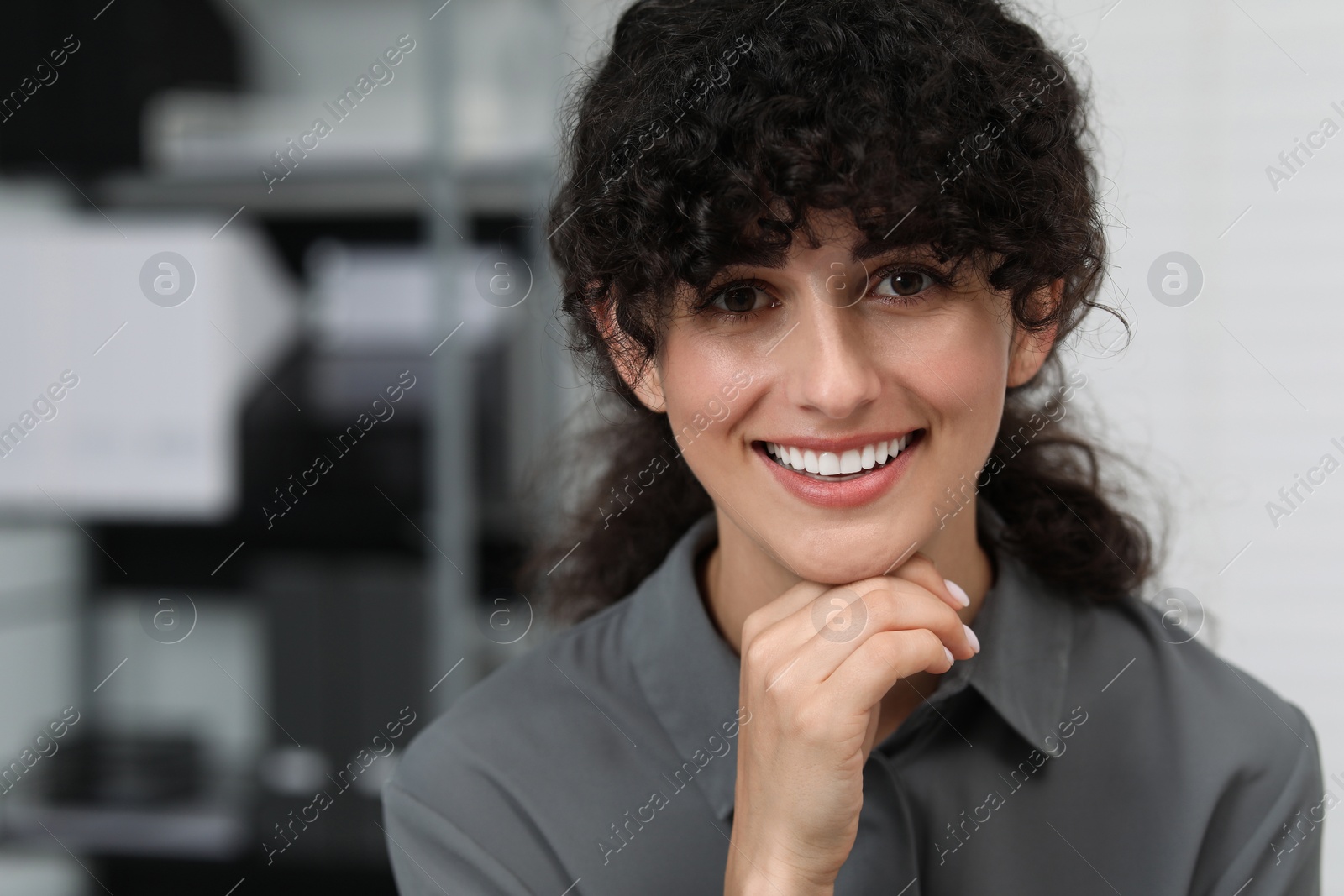 Photo of Portrait of confident entrepreneur indoors. Beautiful lady with curly hair smiling and looking into camera. Space for text