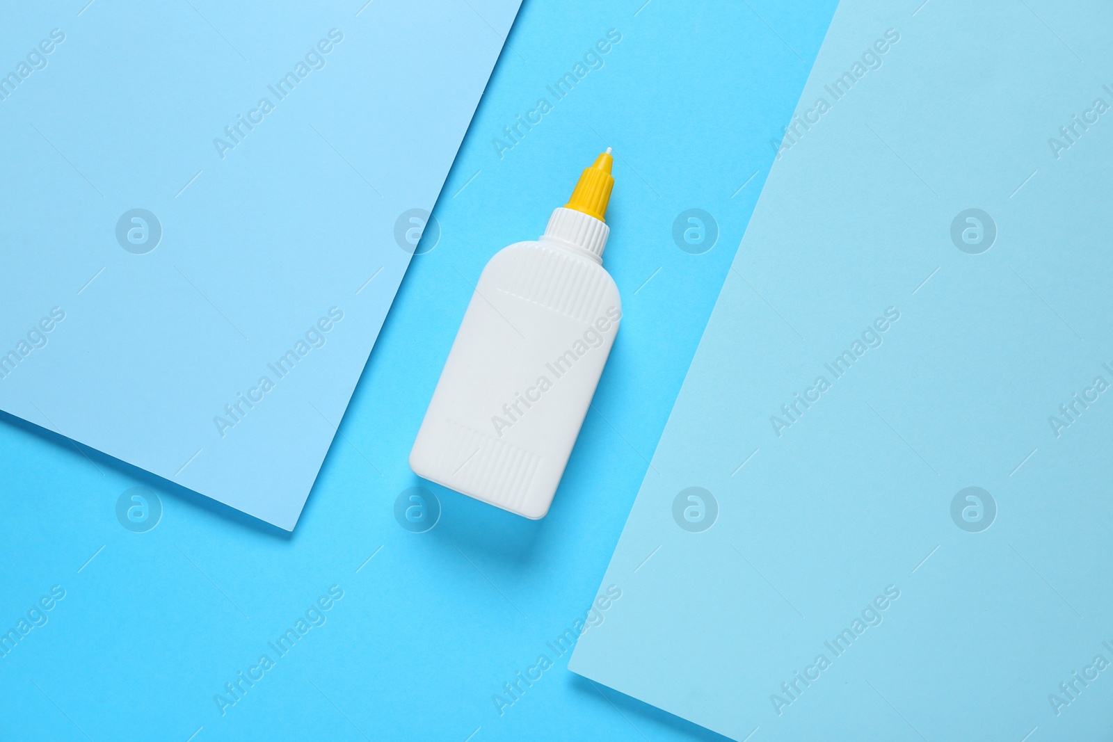 Photo of Bottle of glue and paper on light blue background, flat lay