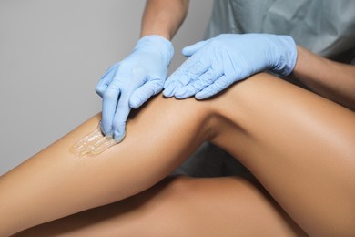 Young woman undergoing hair removal procedure on legs with sugaring paste in salon, closeup