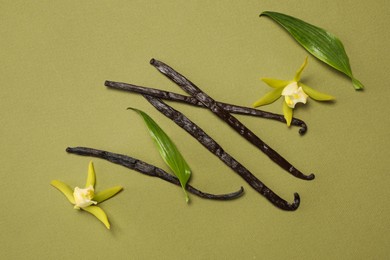 Photo of Vanilla pods, beautiful flowers and green leaves on olive color background, top view