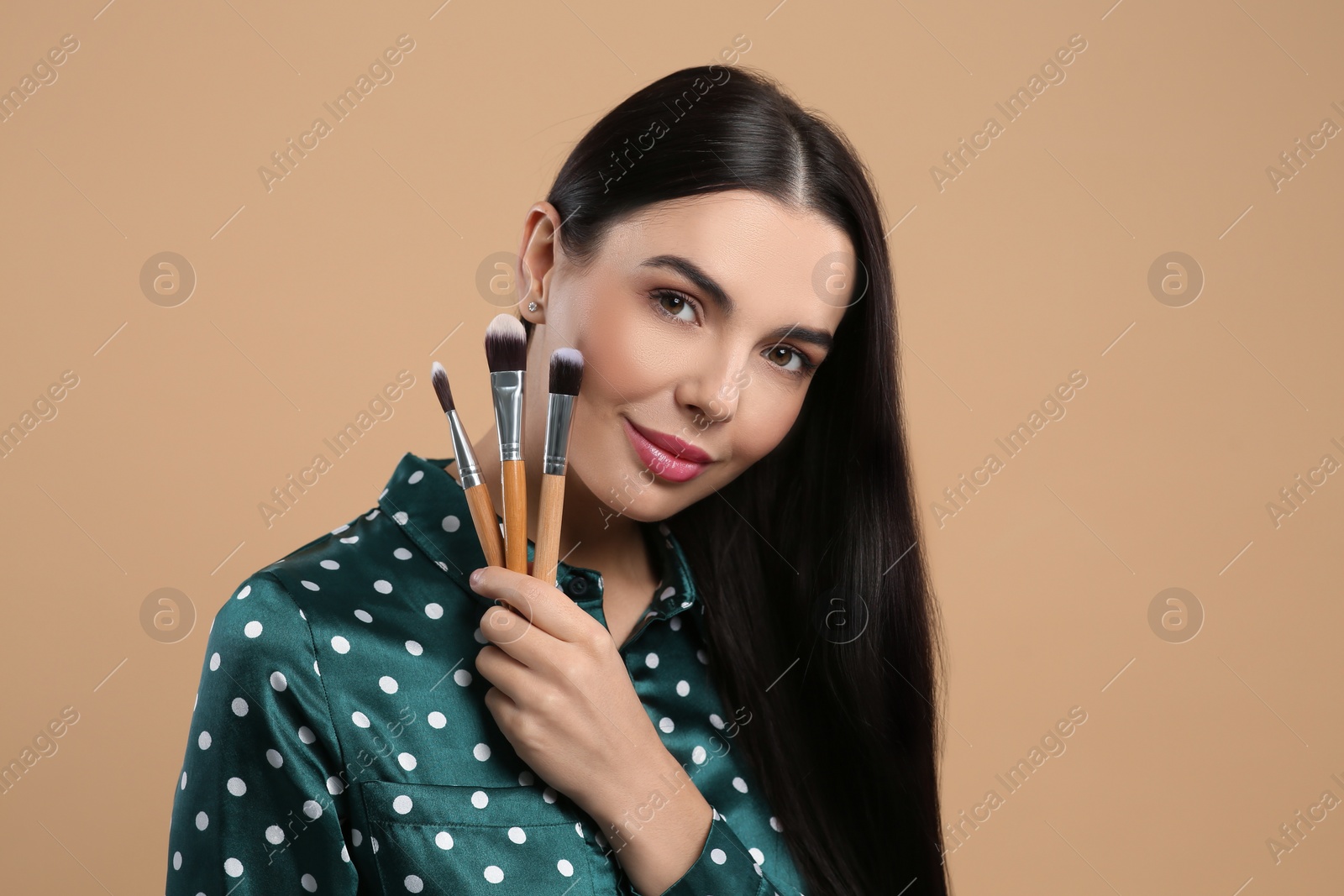 Photo of Beautiful woman with different makeup brushes on light brown background