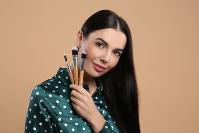 Beautiful woman with different makeup brushes on light brown background