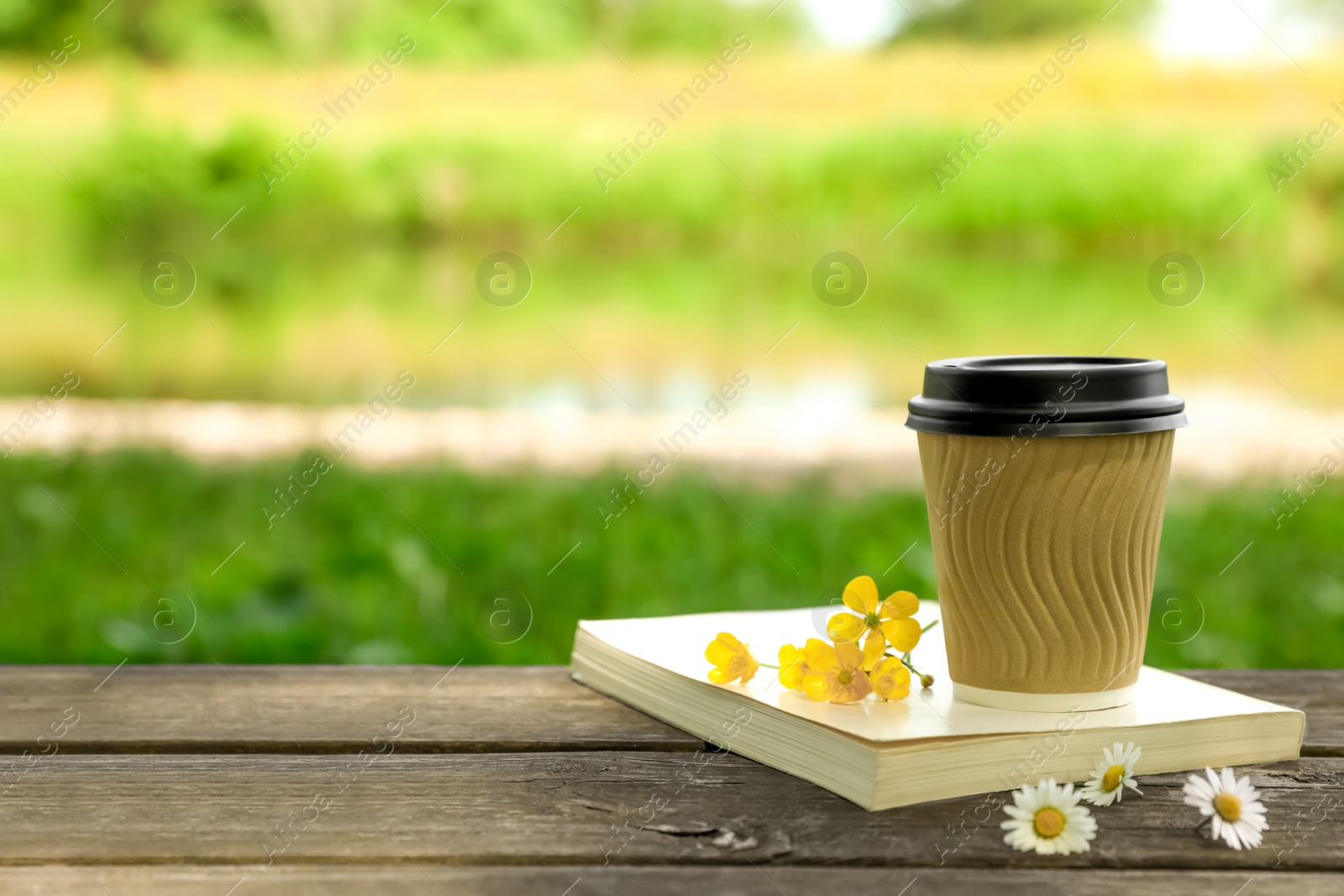 Photo of Paper coffee cup, flowers and book on wooden table outdoors, space for text