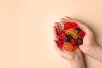 Photo of Woman holding pile of delicious gummy fruit shaped candies on beige background, top view. Space for text