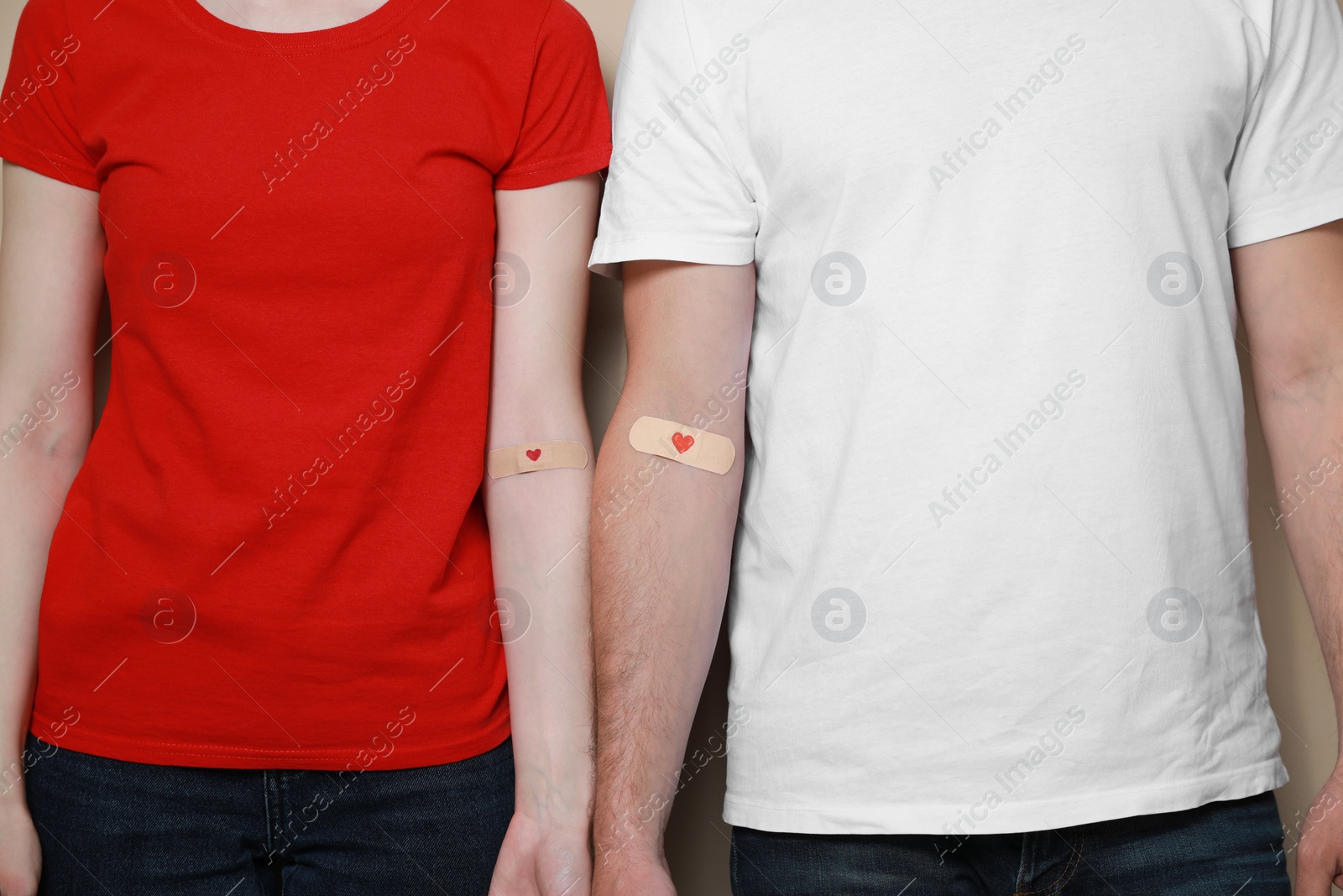 Photo of Blood donation concept. Couple with adhesive plasters on arms against beige background, closeup