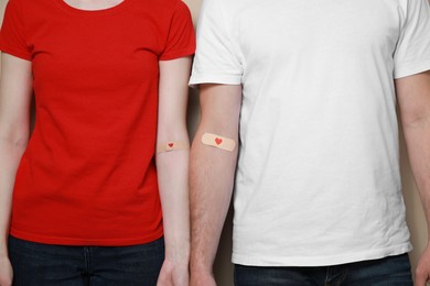 Blood donation concept. Couple with adhesive plasters on arms against beige background, closeup