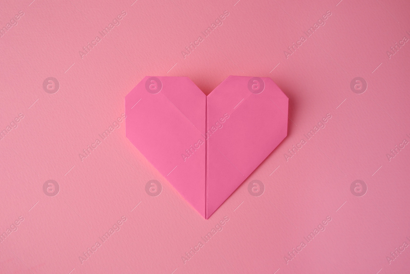 Photo of Origami art. Paper heart on pink background, top view