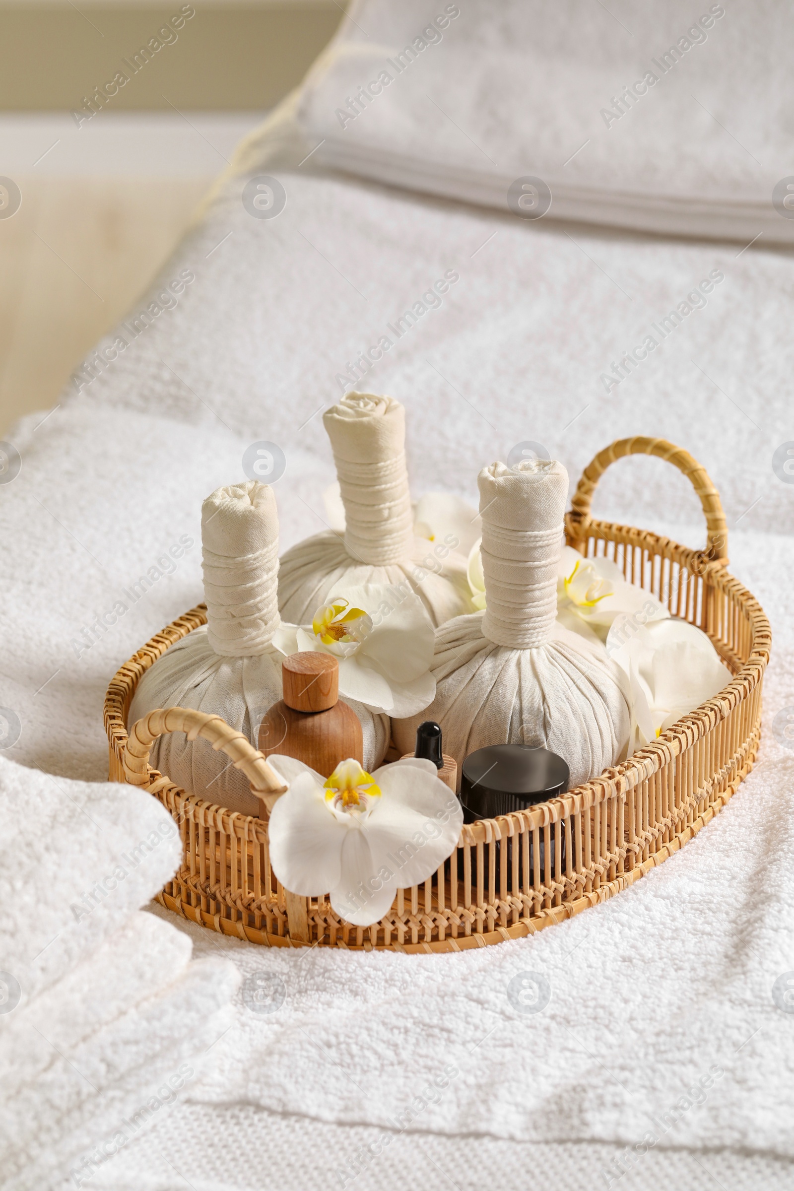 Photo of Wicker tray with herbal bags and other spa products on white bath towel