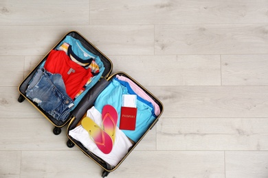 Packed suitcase with summer clothes and passport on wooden background, top view. Space for text