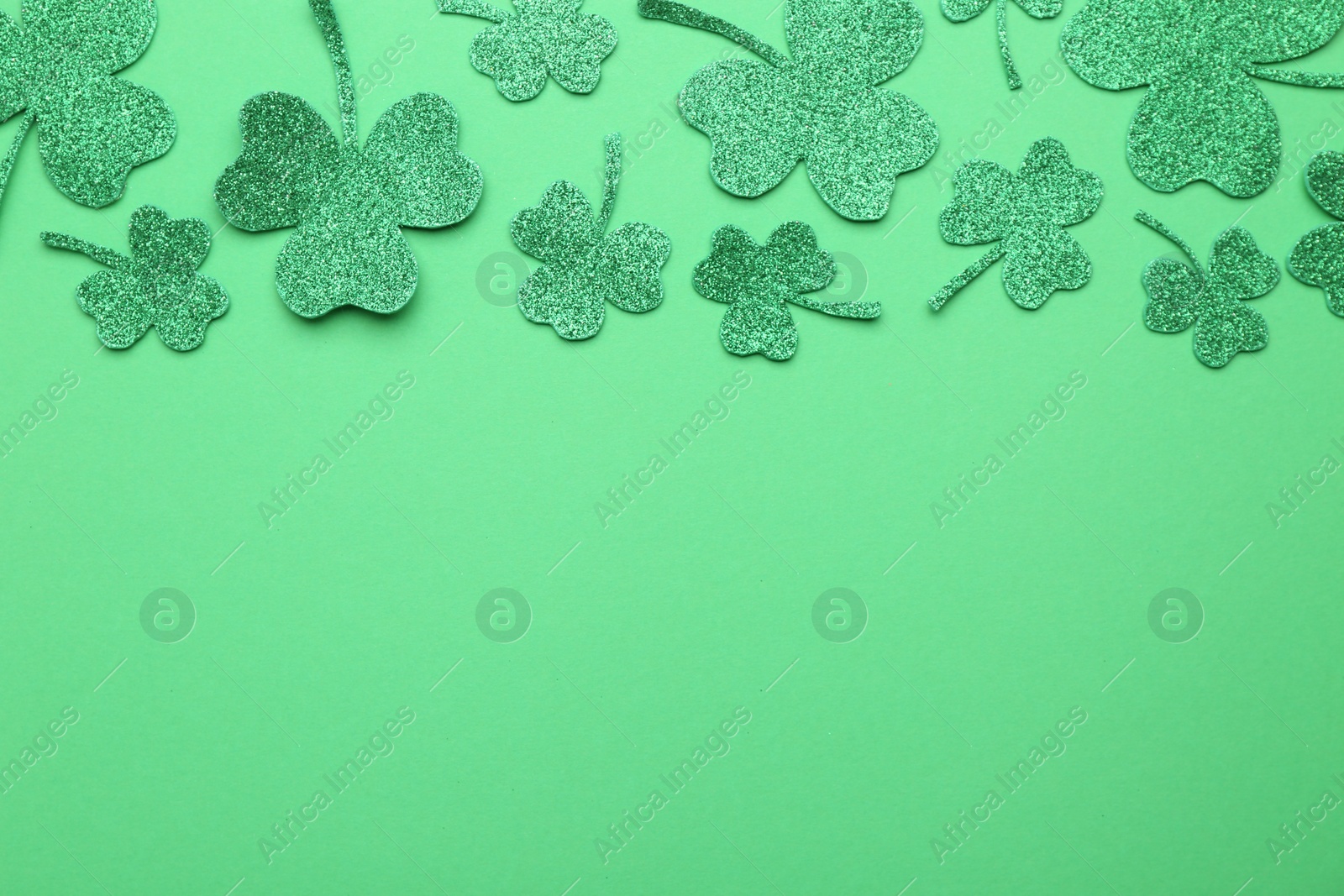 Photo of St. Patrick's day. Shiny decorative clover leaves on green background, flat lay. Space for text