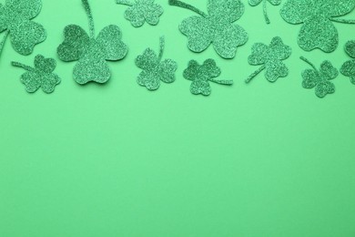 Photo of St. Patrick's day. Shiny decorative clover leaves on green background, flat lay. Space for text