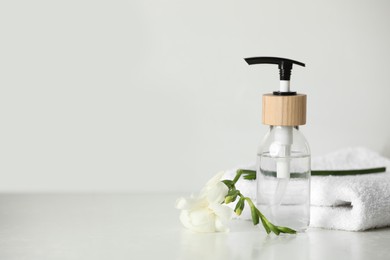 Bottle with dispenser cap, towel and beautiful flower on white table. Space for text