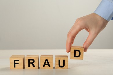 Photo of Woman making word Fraud with wooden cubes at white table, closeup. Space for text
