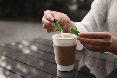 Photo of Woman adding sugar to aromatic coffee in paper cup at table, closeup