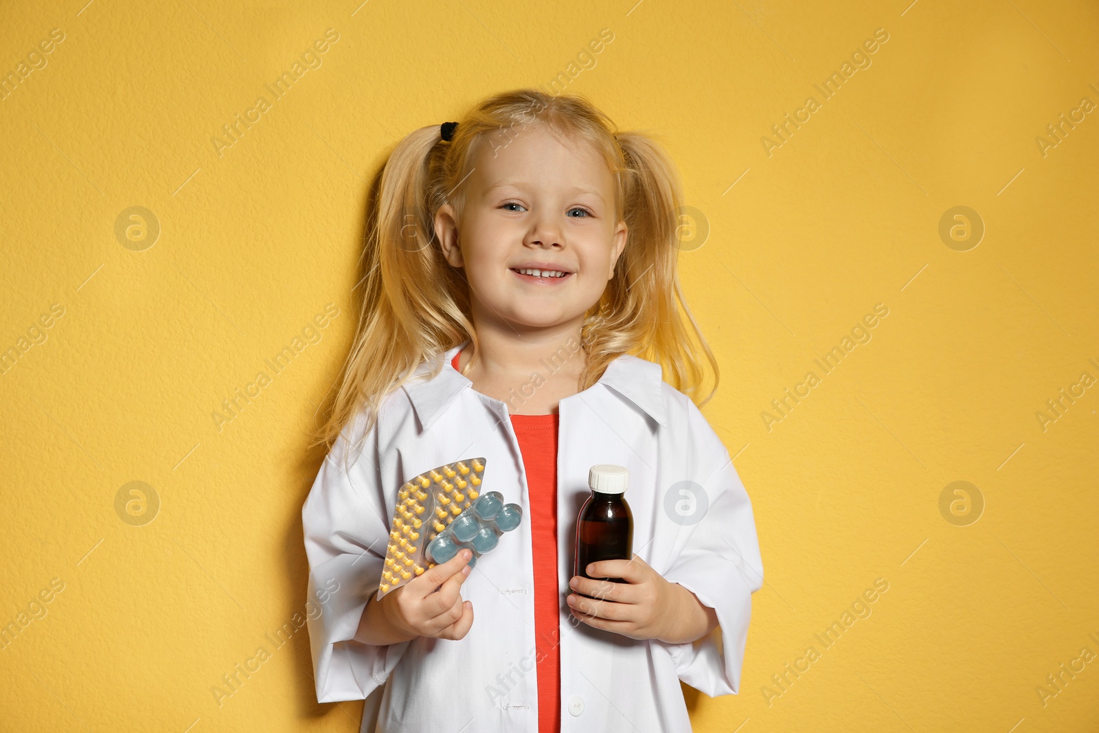 Photo of Cute little child in doctor coat with medications on color background
