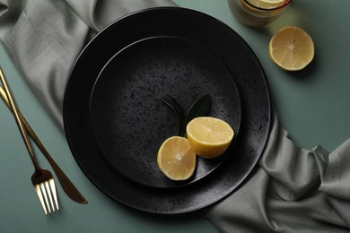 Photo of Stylish table setting. Plates, cutlery and lemon on olive background, flat lay