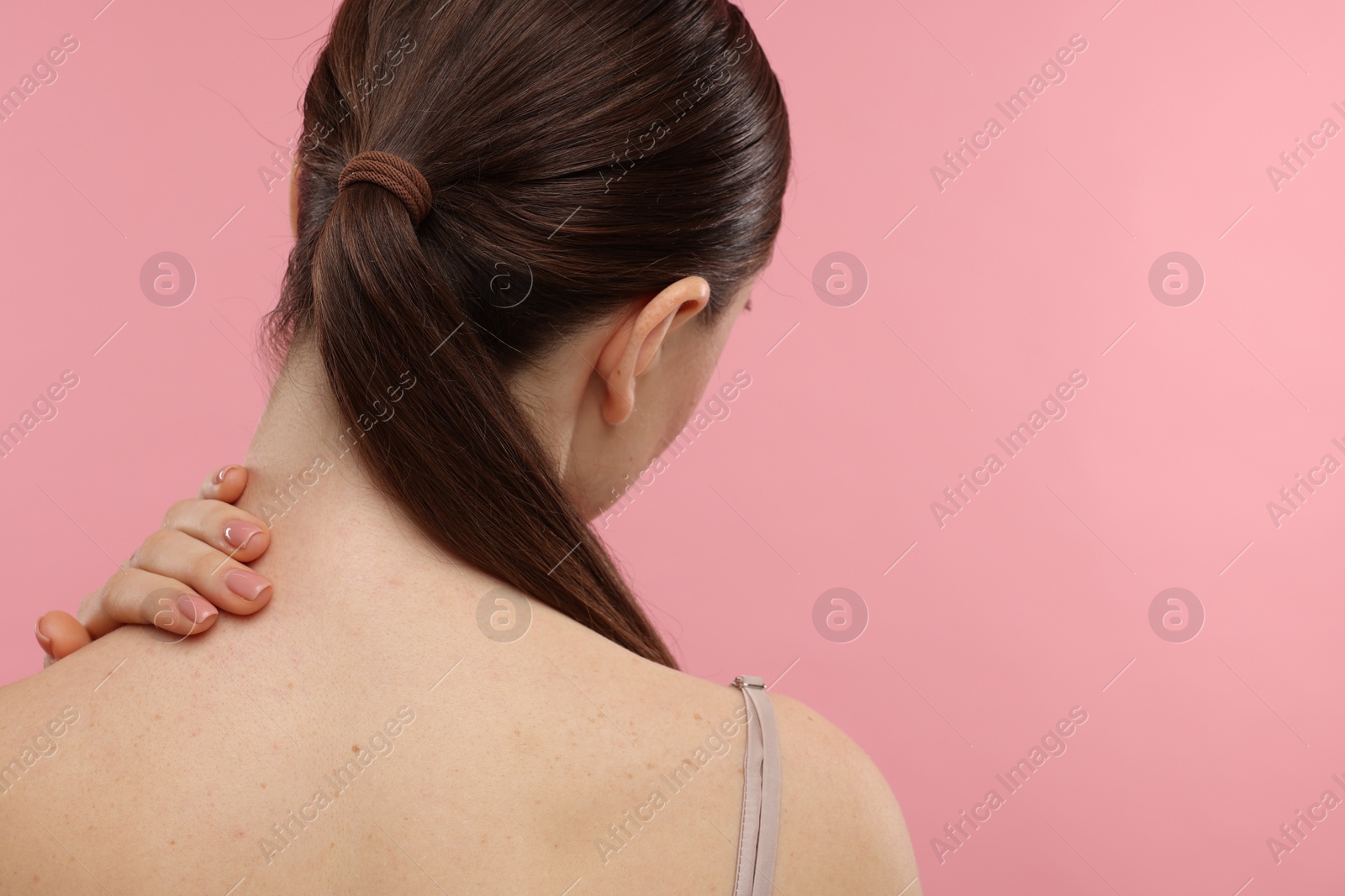 Photo of Woman touching her neck on pink background, back view. Space for text