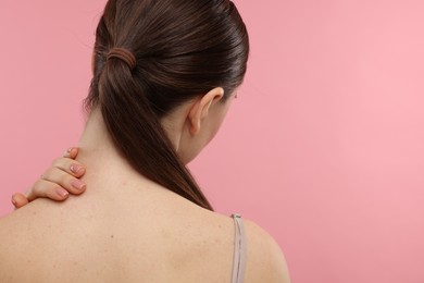 Woman touching her neck on pink background, back view. Space for text