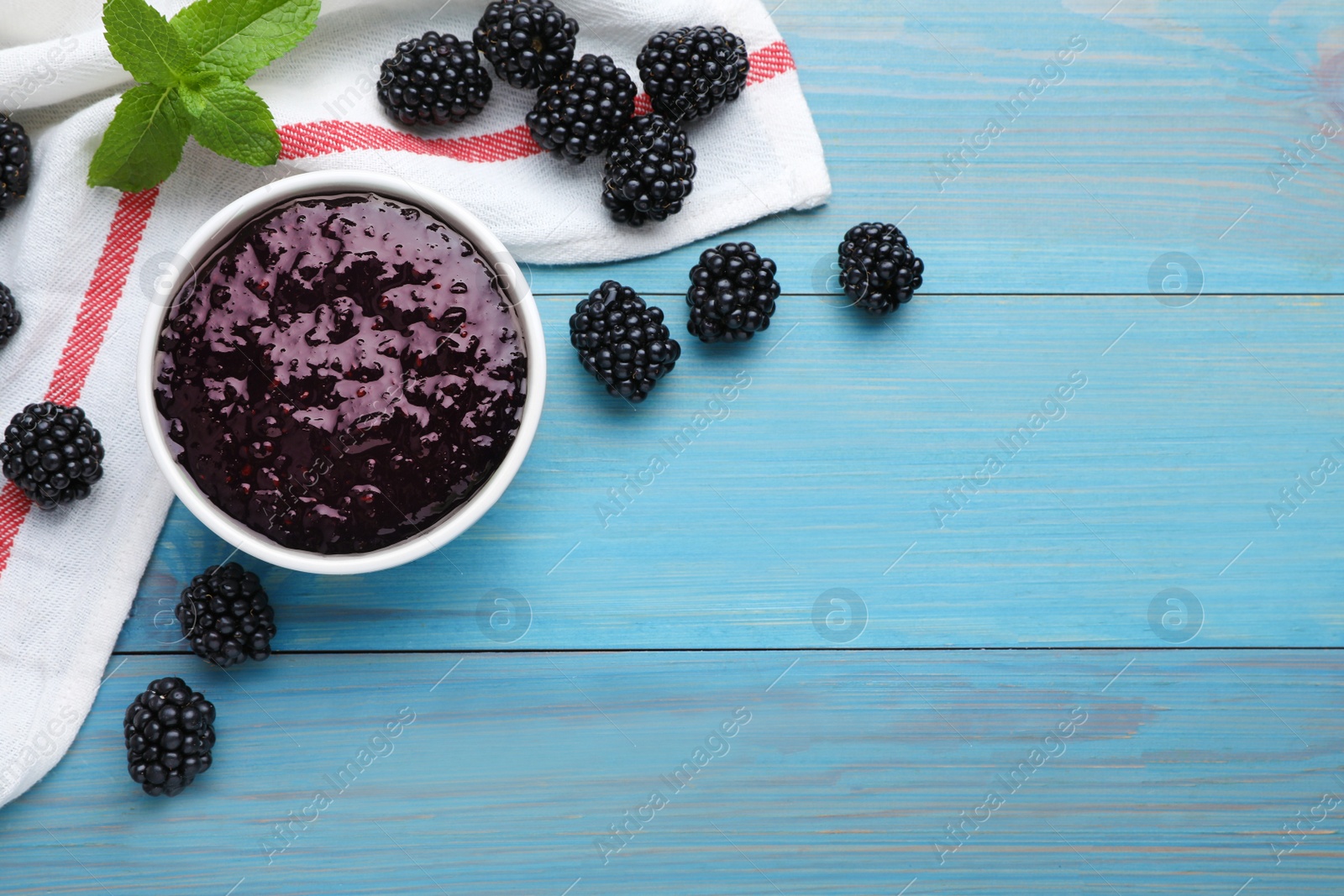 Photo of Blackberry puree in bowl and fresh berries on light blue wooden table, flat lay. Space for text