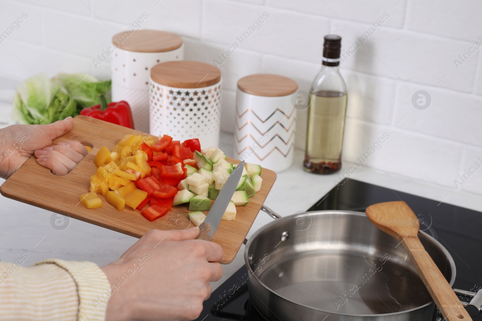 Photo of Woman putting cut vegetables into saute pan in kitchen, closeup