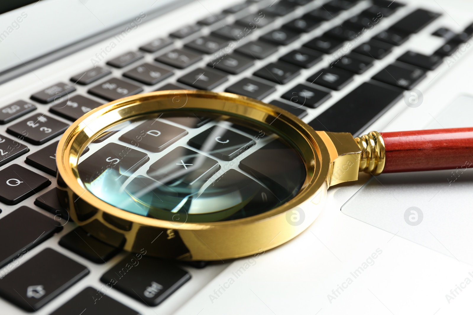 Photo of Magnifying glass on keyboard of modern laptop, closeup. Search concept