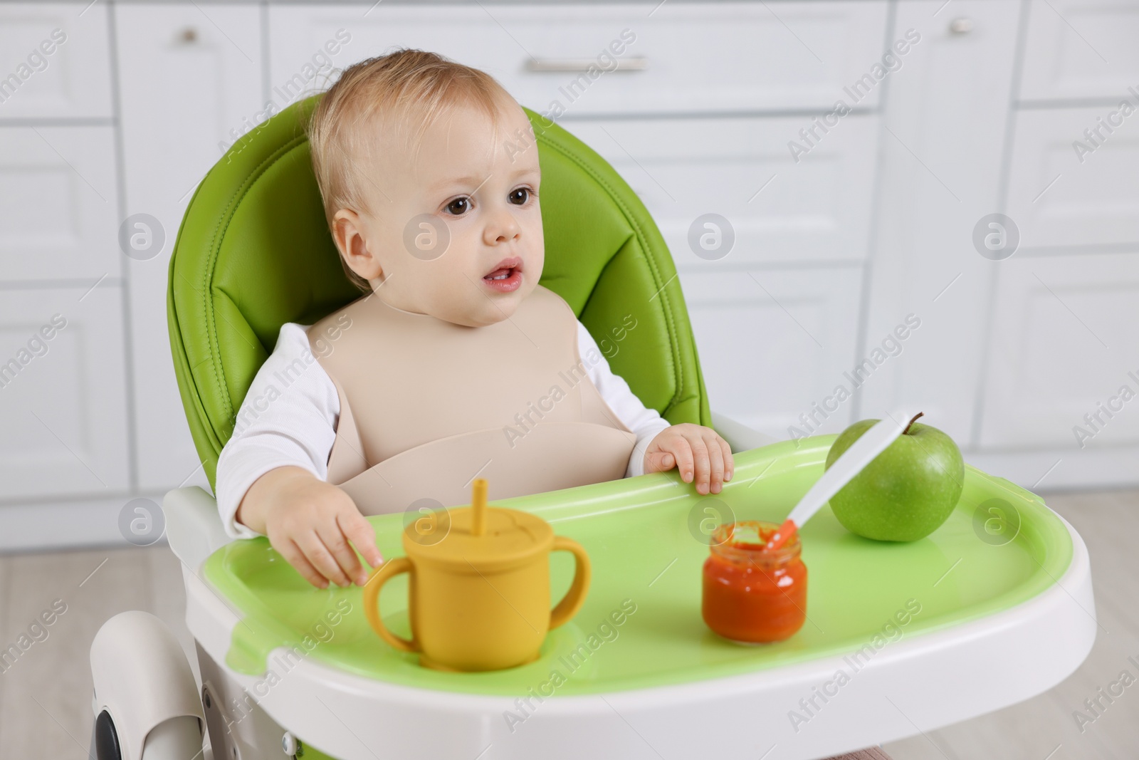 Photo of Cute little baby with healthy food in high chair at home